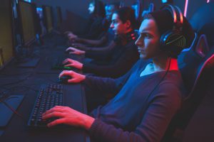 Serious concentrated esports player concentrated on game wearing wired headset sitting at table and playing online multiplayer game