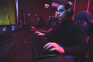 Serious focused multi-ethnic e-sports gamers in dark clothes sitting at table and playing online game via network